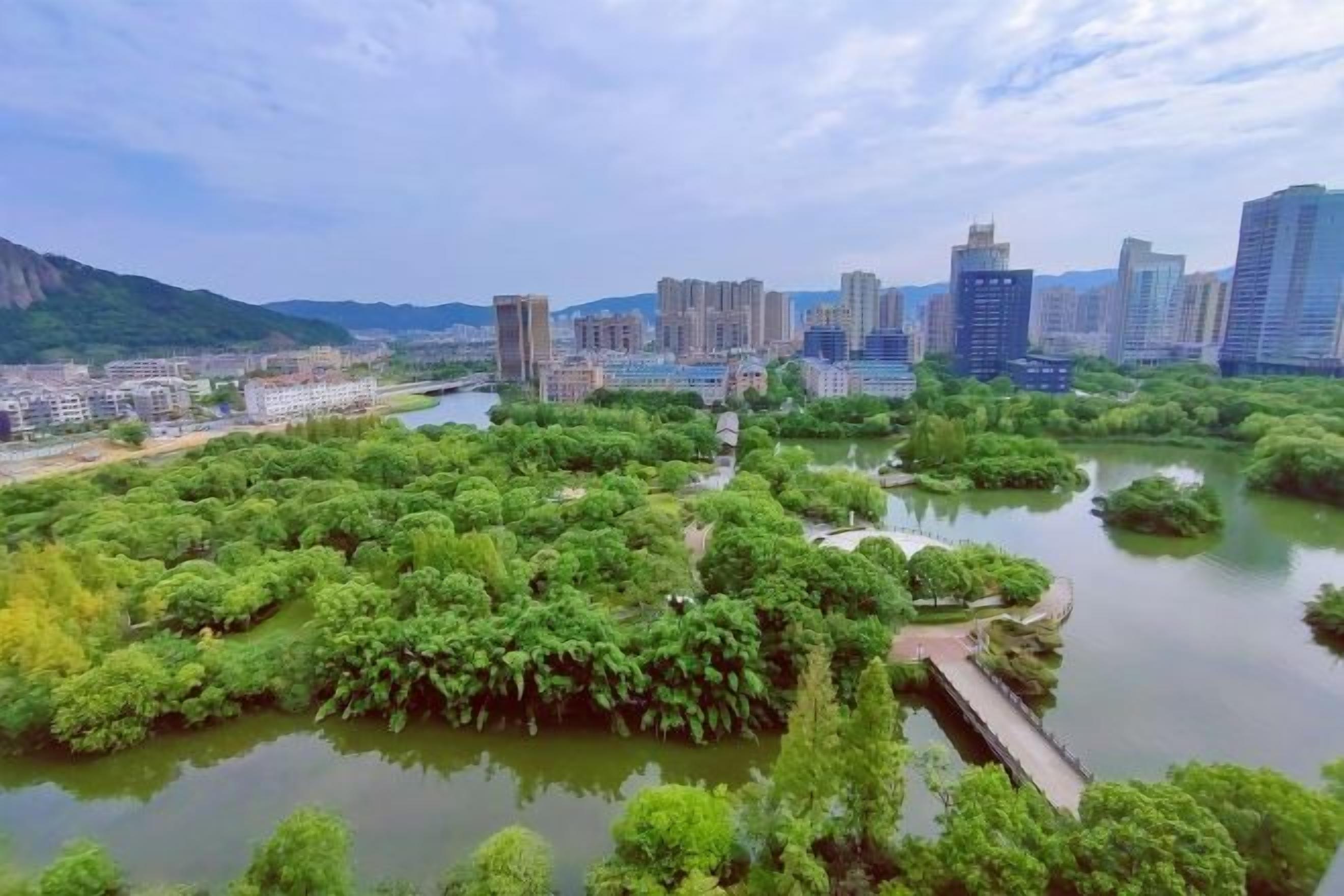 A cityscape with a river, dense greenery, and modern buildings.
