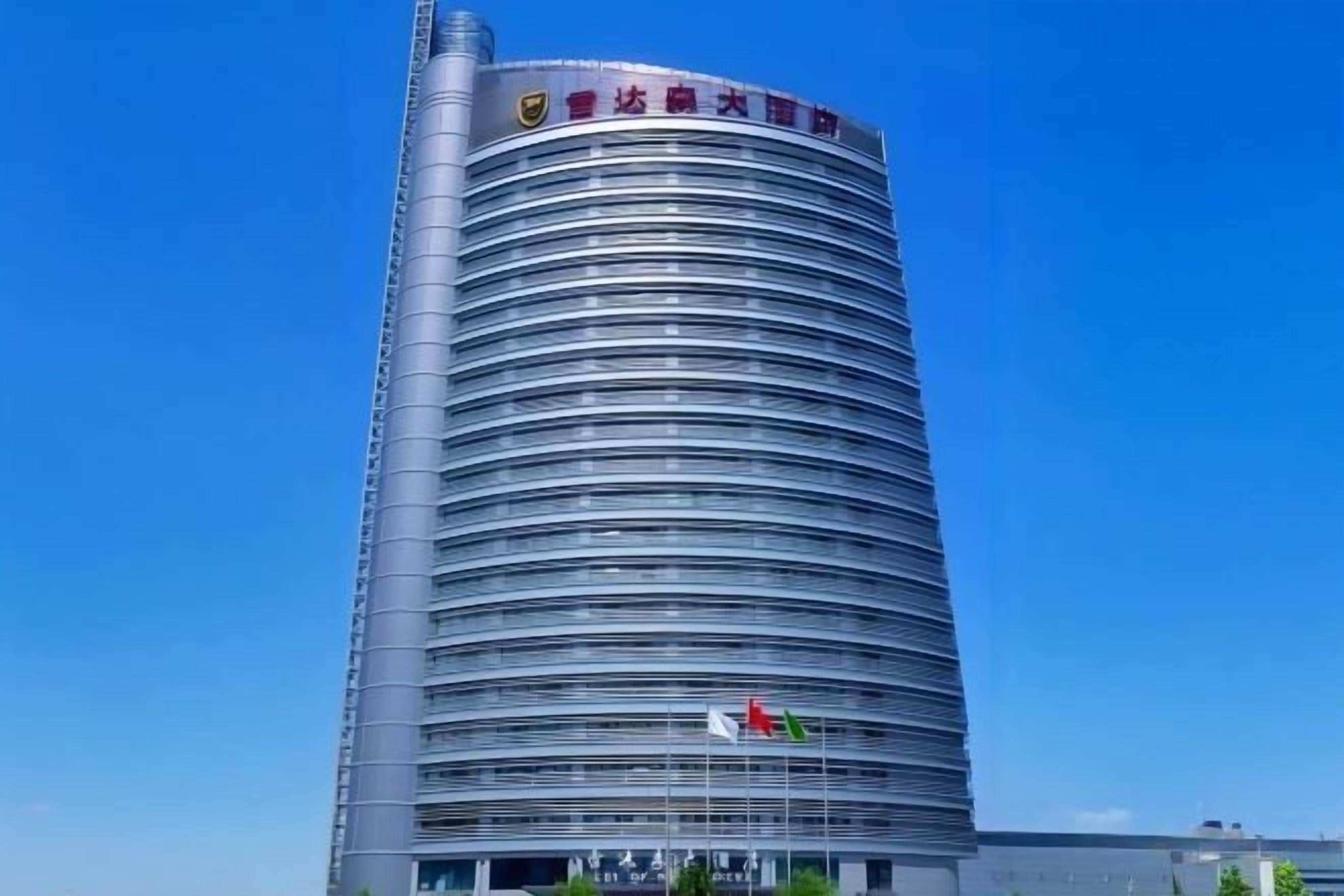 A tall, cylindrical building with horizontal lines, a flag, and a sign with Chinese characters.