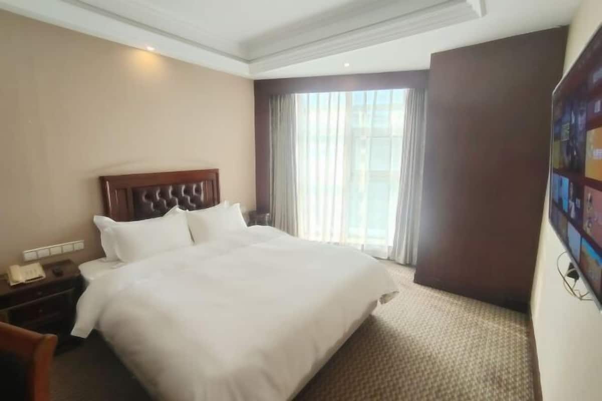 Una habitación de hotel con una cama grande, una mesita de noche, un escritorio y una ventana con cortinas.