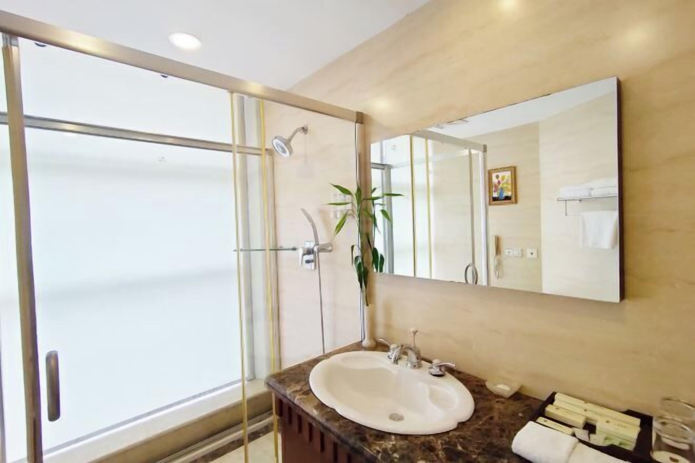 A modern bathroom with a glass shower enclosure, a marble countertop sink, and a large mirror.