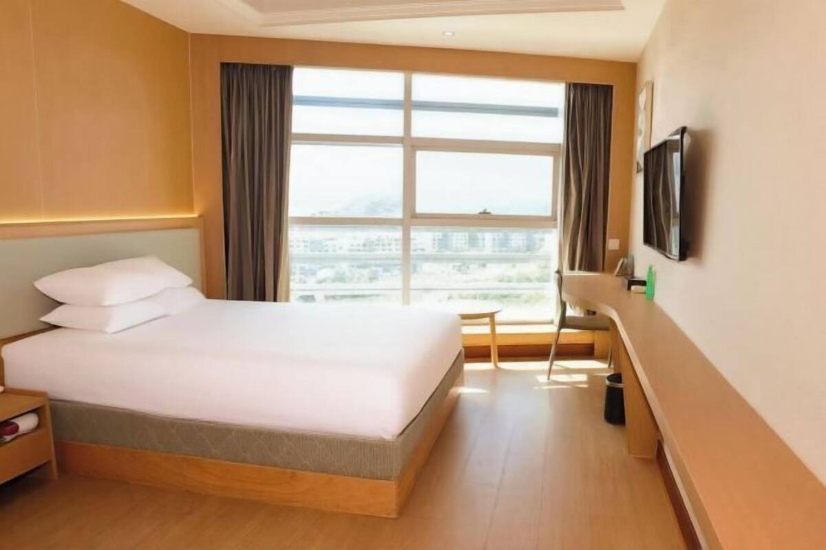 Una habitación de hotel con una cama grande, un televisor montado en la pared y una ventana con cortinas.