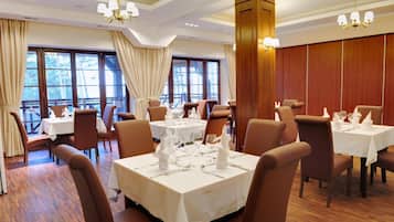 A restaurant with multiple tables set for dining, large windows, and wooden paneling on the walls.