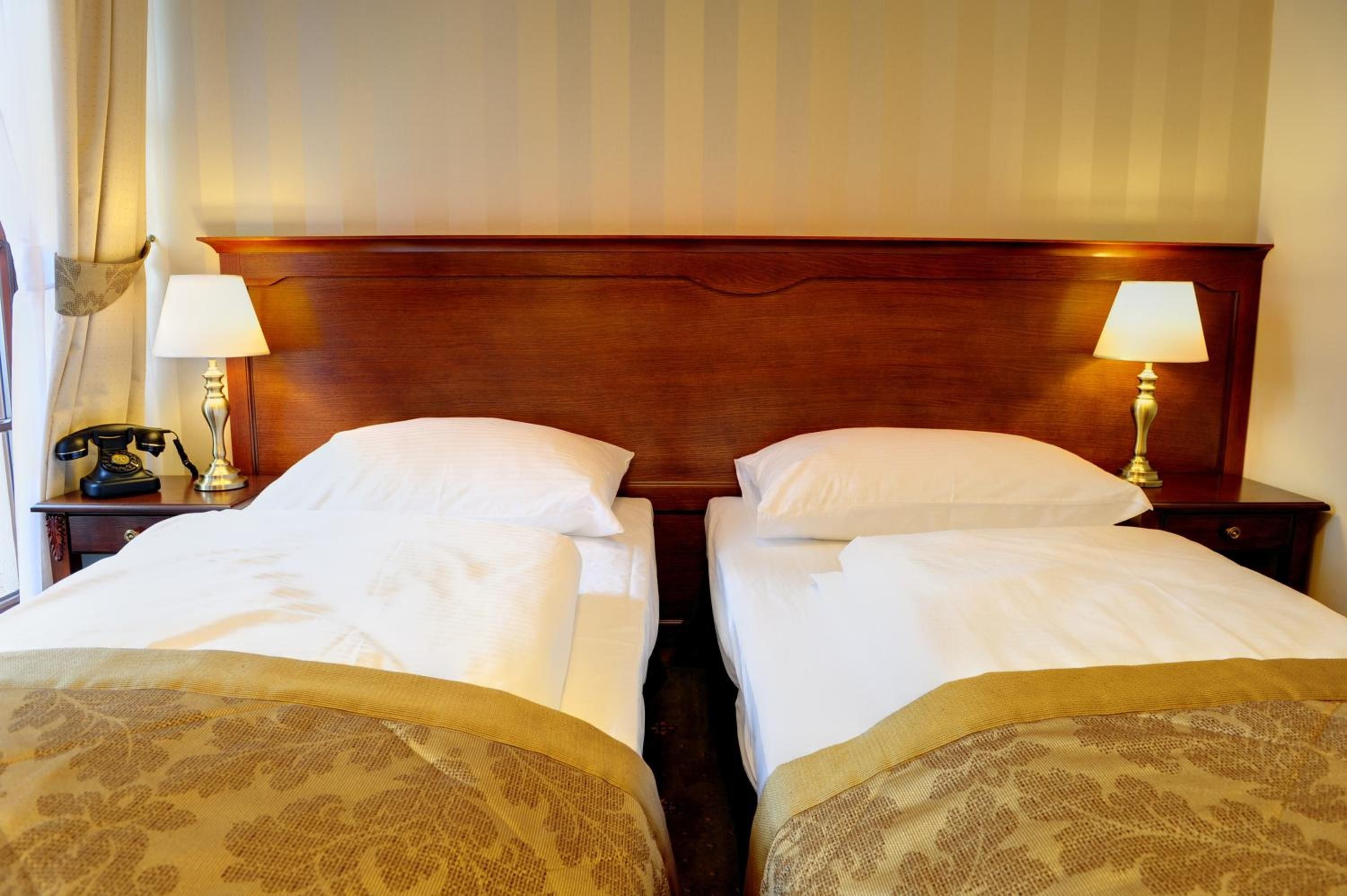 A hotel room with two single beds, wooden headboards, bedside lamps, a telephone, and a window with curtains.