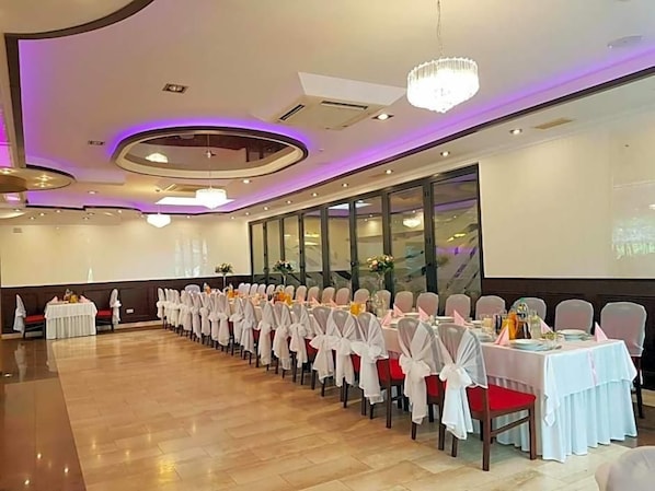 A banquet hall with rows of tables, chairs, and a large screen.