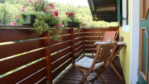 Una terraza de madera con una mesa y sillas, rodeada por un cerco de madera y macetas con flores.