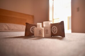 A bed with a wooden headboard and a white pillow. There are three toiletries on the bed: a bottle of shampoo, a bottle of lotion, and a bar of soap. - Hotel Casa Santo Tomás (Oaxaca)