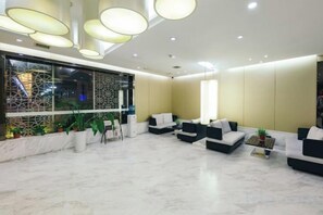 Een moderne lobby met zithoeken, een receptiebalie en een groot raam met planten.