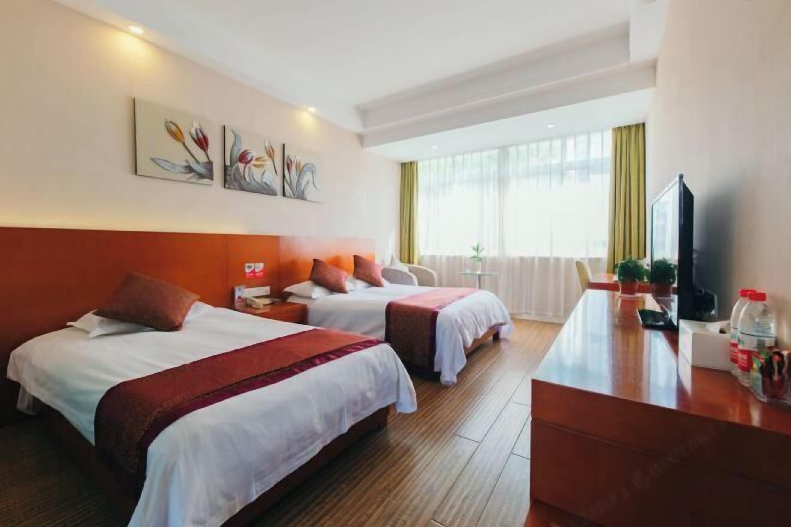 A hotel room with two beds, a desk, a TV, and artwork on the wall.