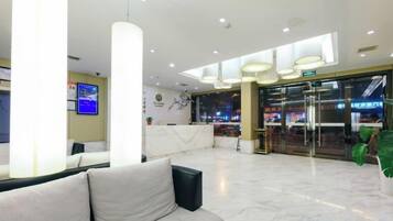 Eine Hotelhalle mit einer Rezeption, einer Sitzecke und einer Treppe zu einer oberen Etage.