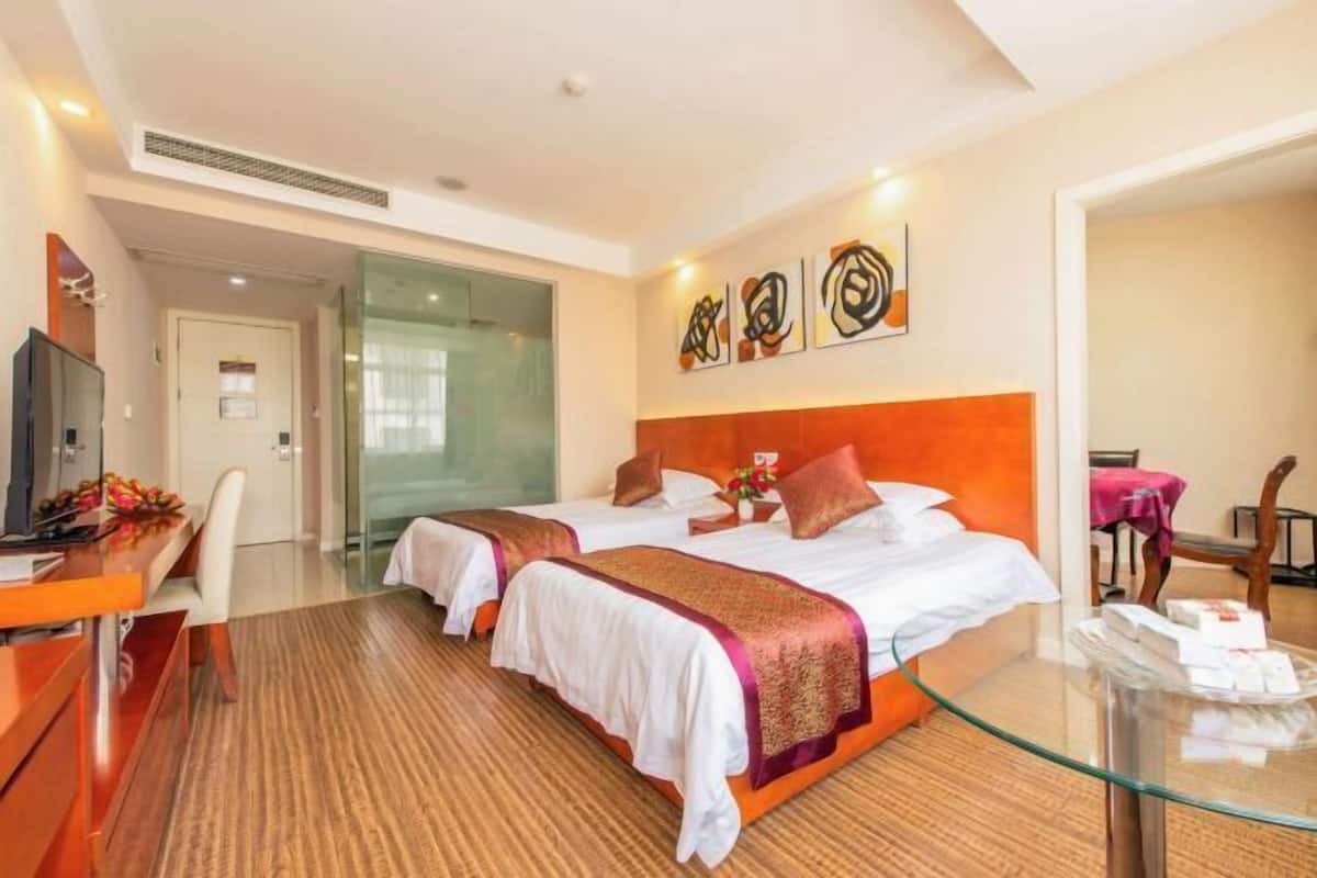 A hotel room with two beds, a desk, a glass table, and artwork on the wall.