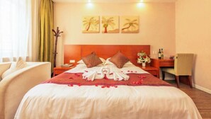 A hotel room with a bed, pillows, a nightstand, a chair, a desk, and a wall with three palm tree paintings. - Xitang Hotel (Jiaxing)