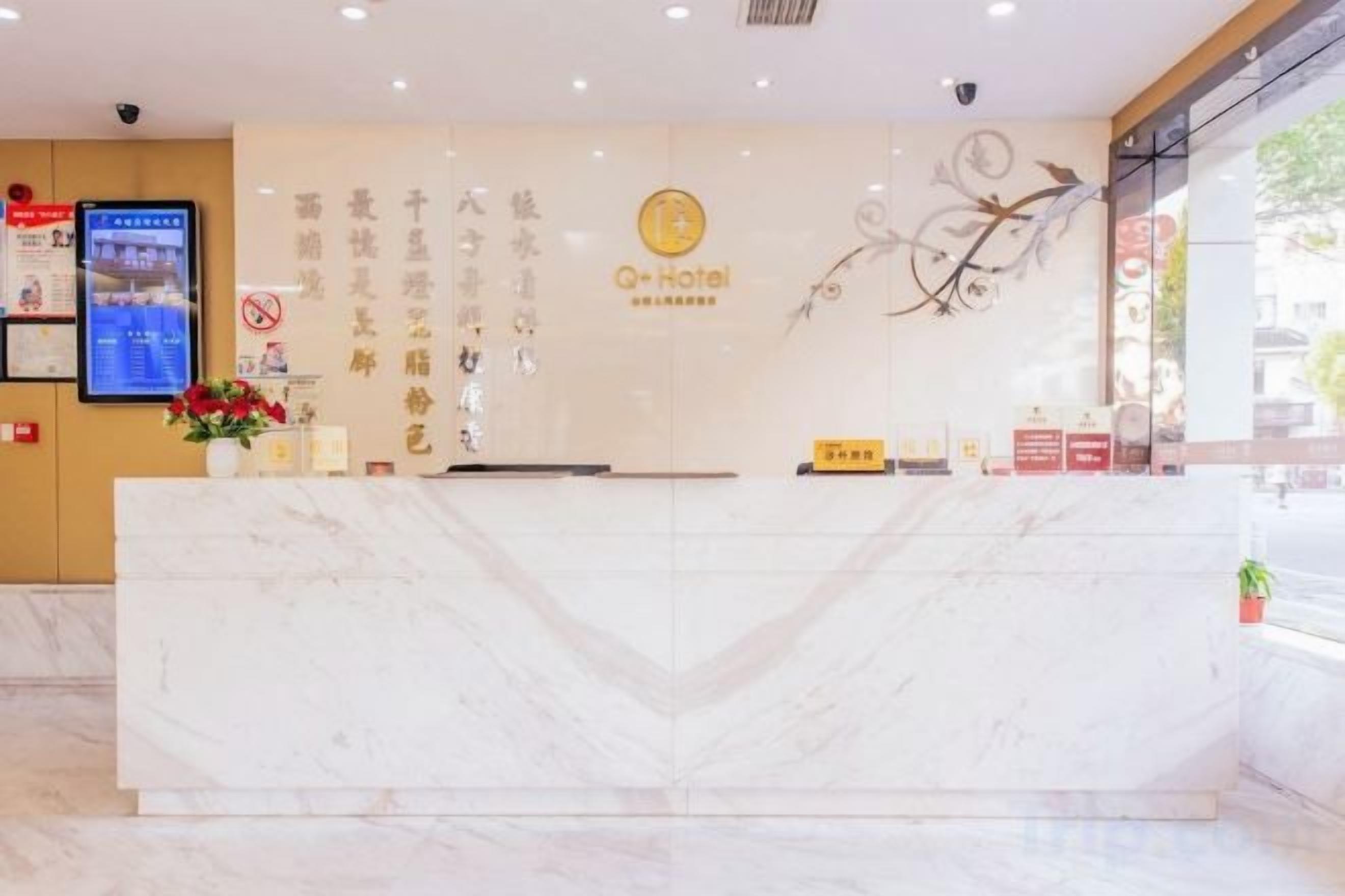 Una recepción de hotel con encimera de mármol, una pantalla digital y una pared con detalles decorativos.