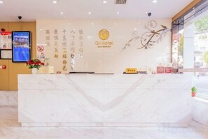 Una recepción de hotel con encimera de mármol, una pantalla digital y una pared con detalles decorativos.