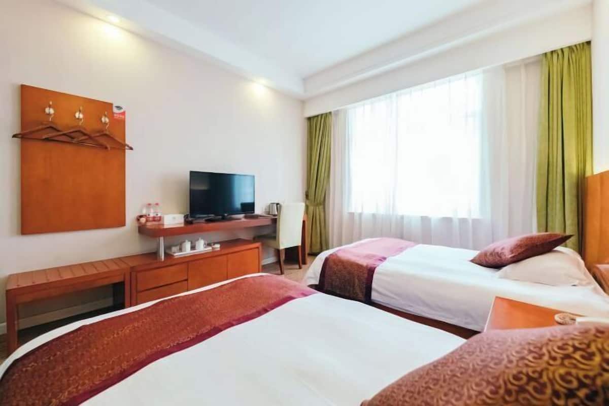 A hotel room with two beds, a TV, a desk, and a wardrobe.