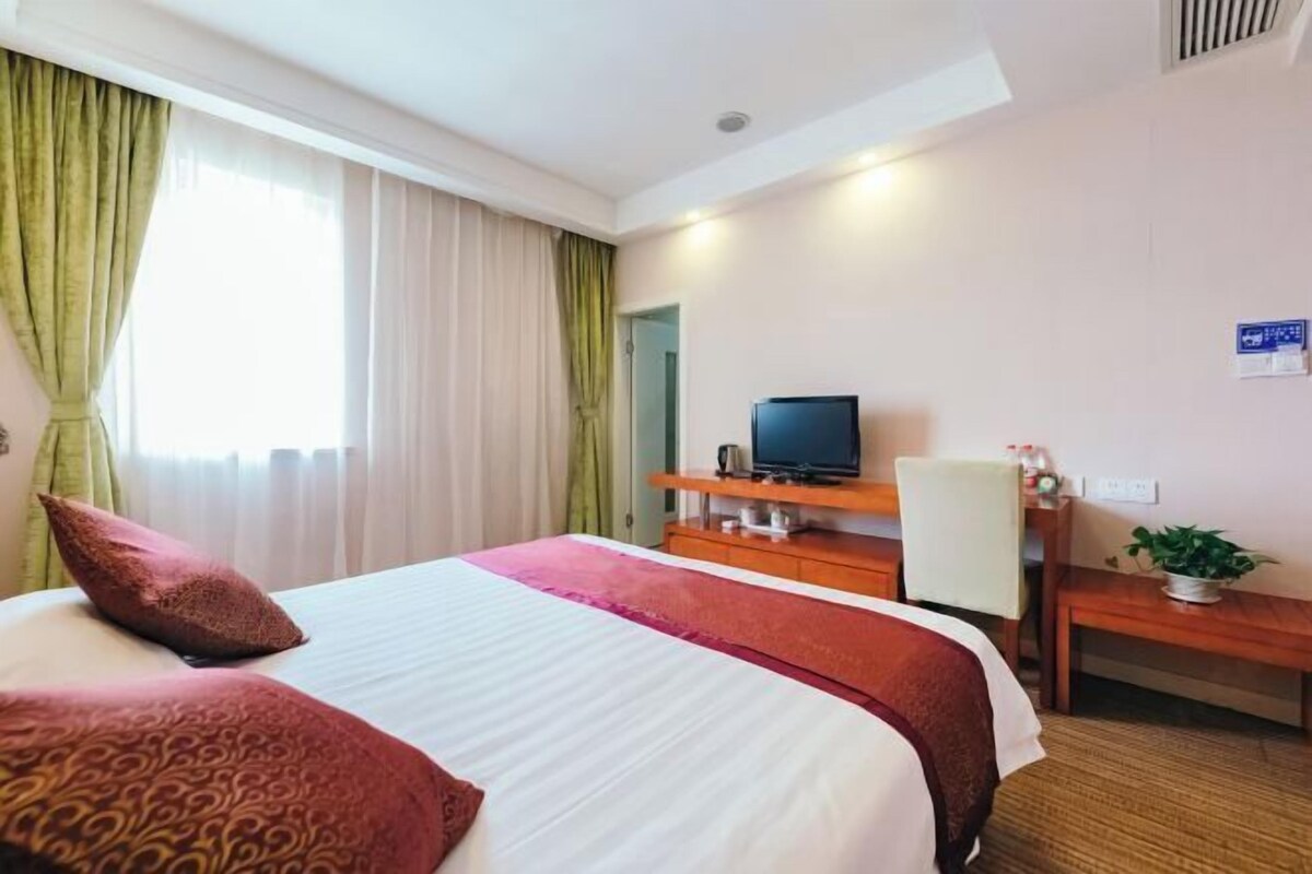 A hotel room with a bed, a television, a desk, and a plant.