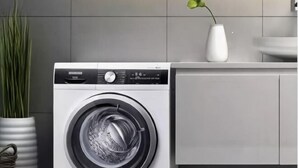 A front-loading washing machine in a modern kitchen with a grey tiled backsplash and a white vase on the counter. - Xitang Hotel (Jiaxing)