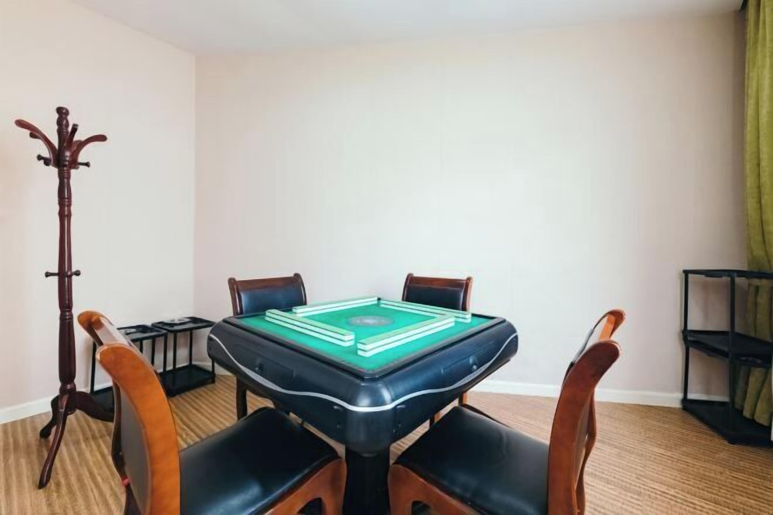 A pool table in a room with four wooden chairs, a coat rack, and a shelf with items.