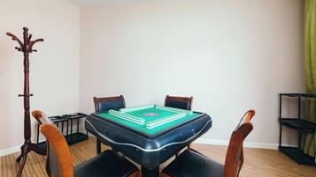 A pool table in a room with four wooden chairs, a coat rack, and a shelf with items.