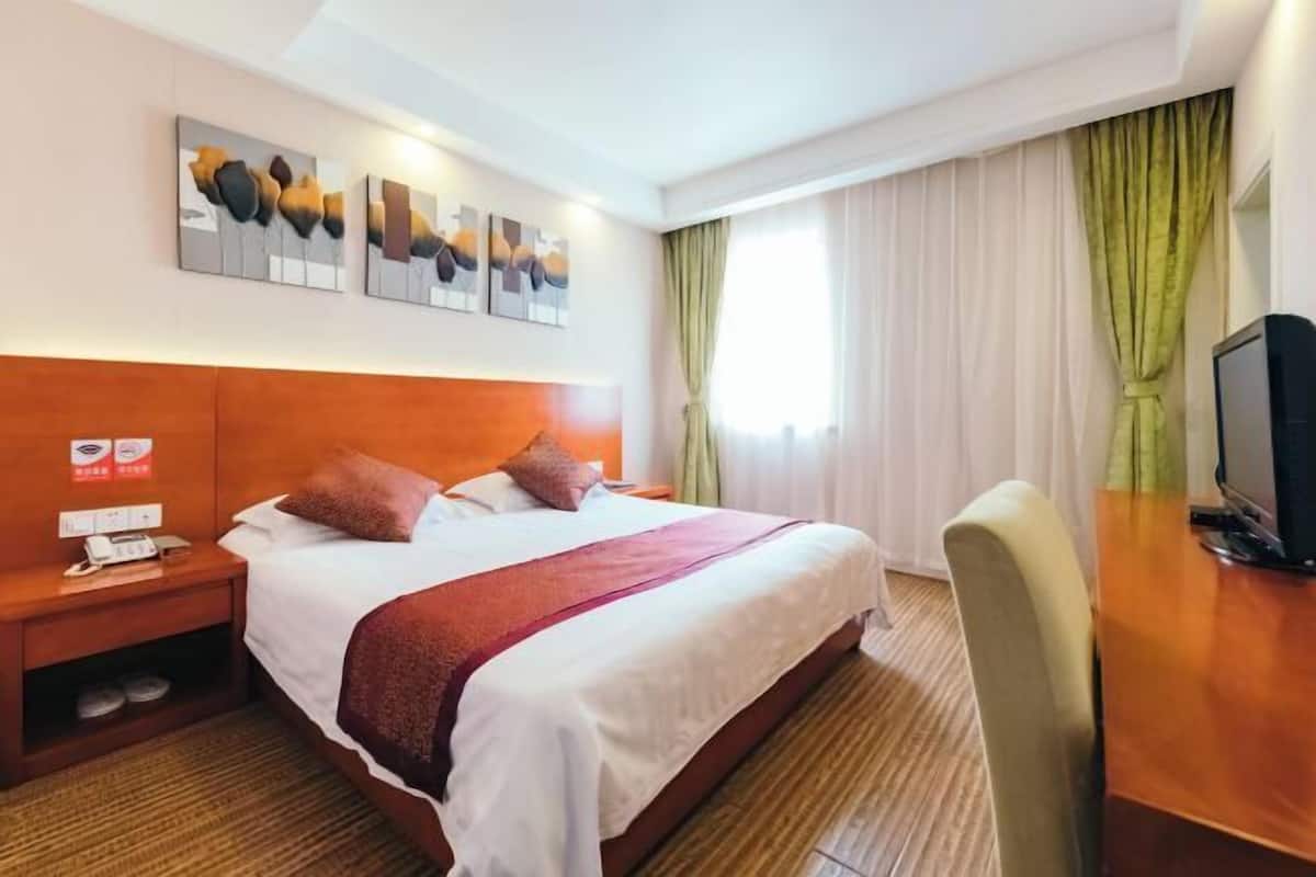 A hotel room with a bed, a desk, a television, and artwork on the wall.