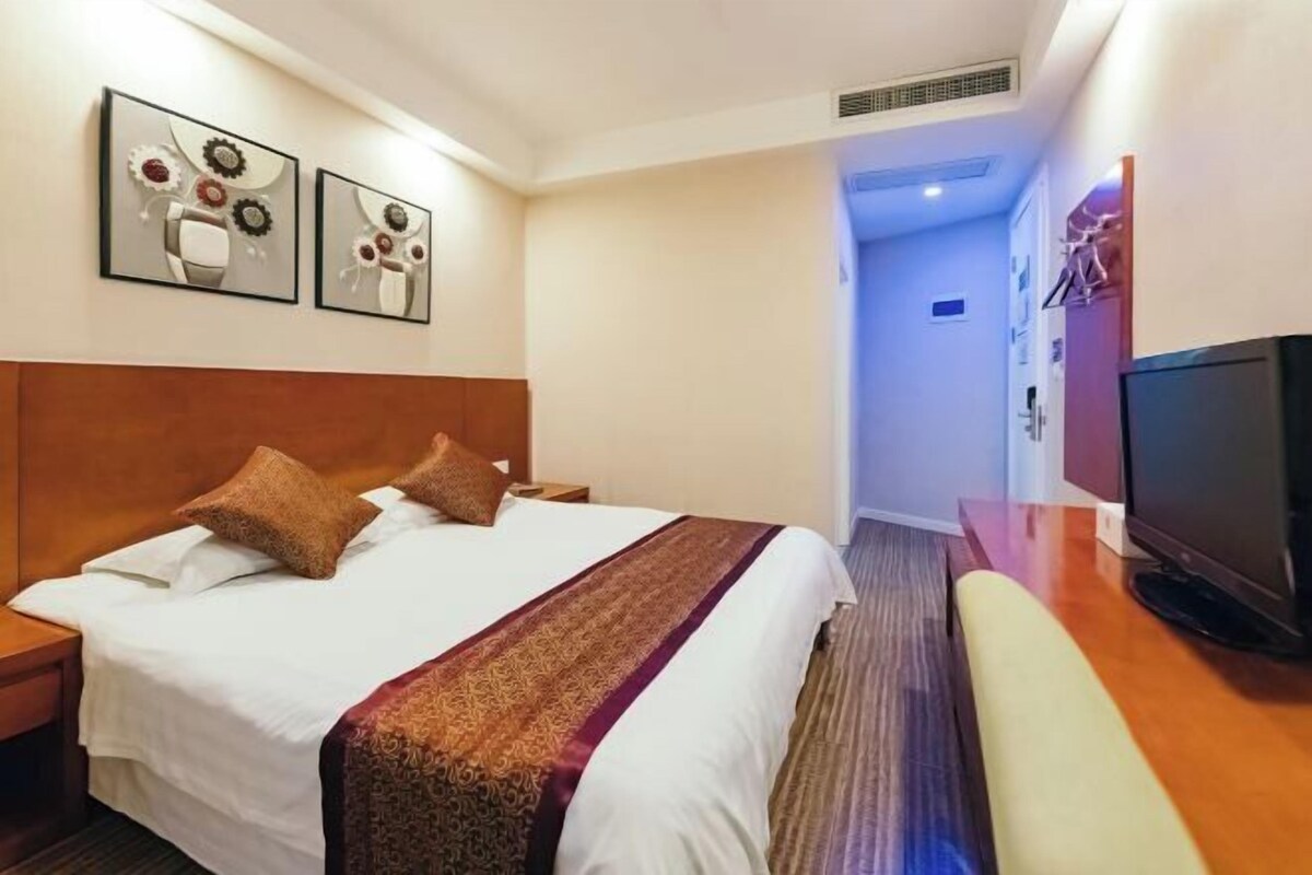 A hotel room with a bed, a TV, a desk, and artwork on the wall.
