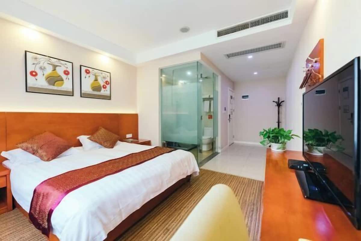 A hotel room with a bed, a desk, a TV, and two wall-mounted paintings.