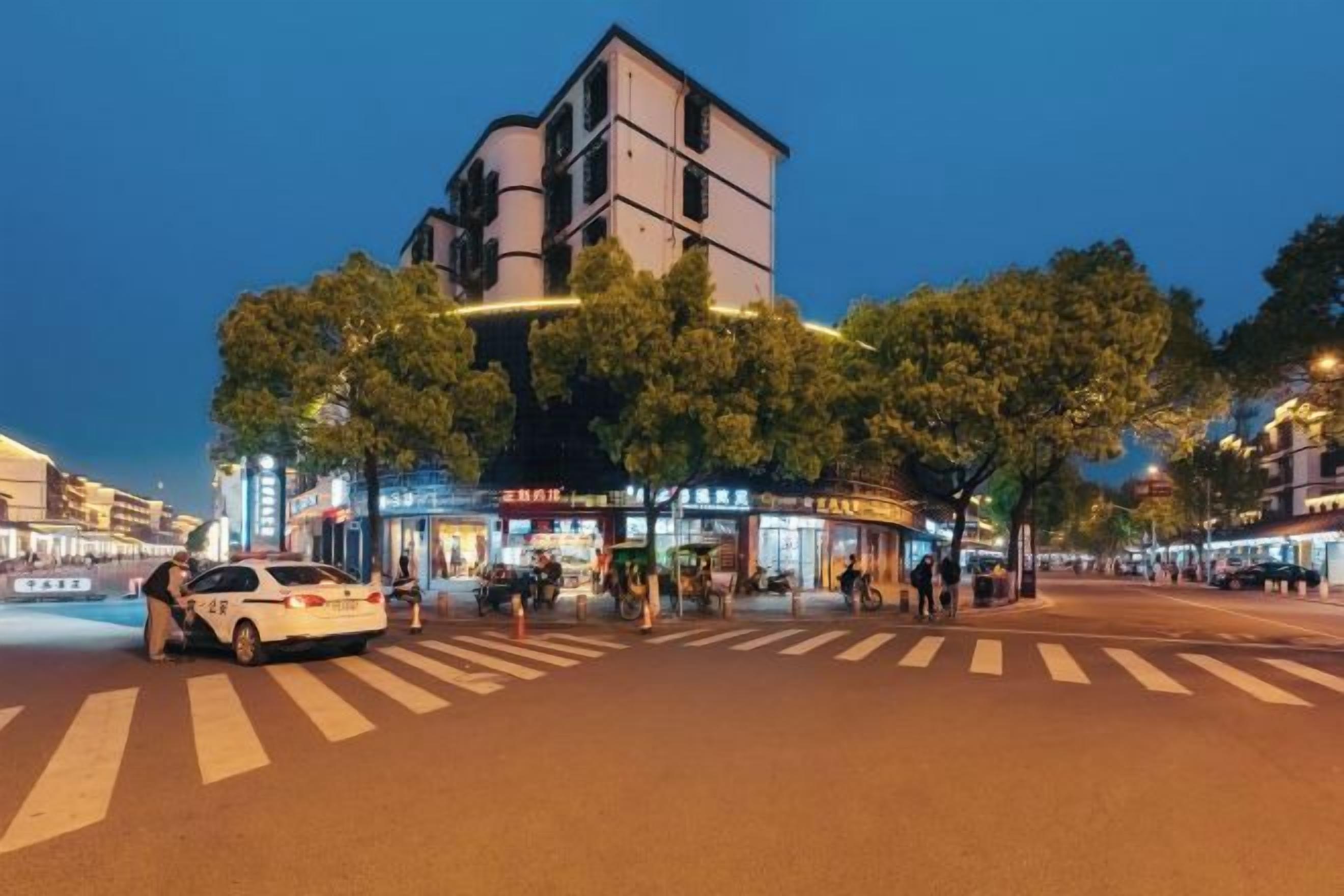 A street scene at night with a crosswalk, trees, and buildings with illuminated signs.