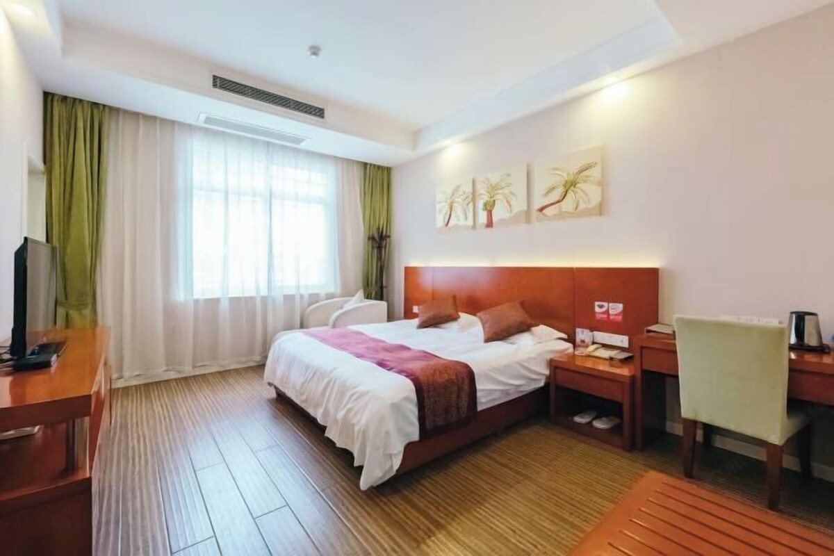 A hotel room with a bed, a desk, a chair, a nightstand, and a window with curtains.
