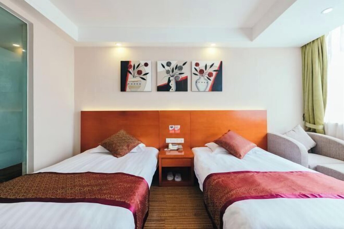 A hotel room with two beds, a wooden headboard, a nightstand with a phone and a lamp, and three wall-mounted paintings.