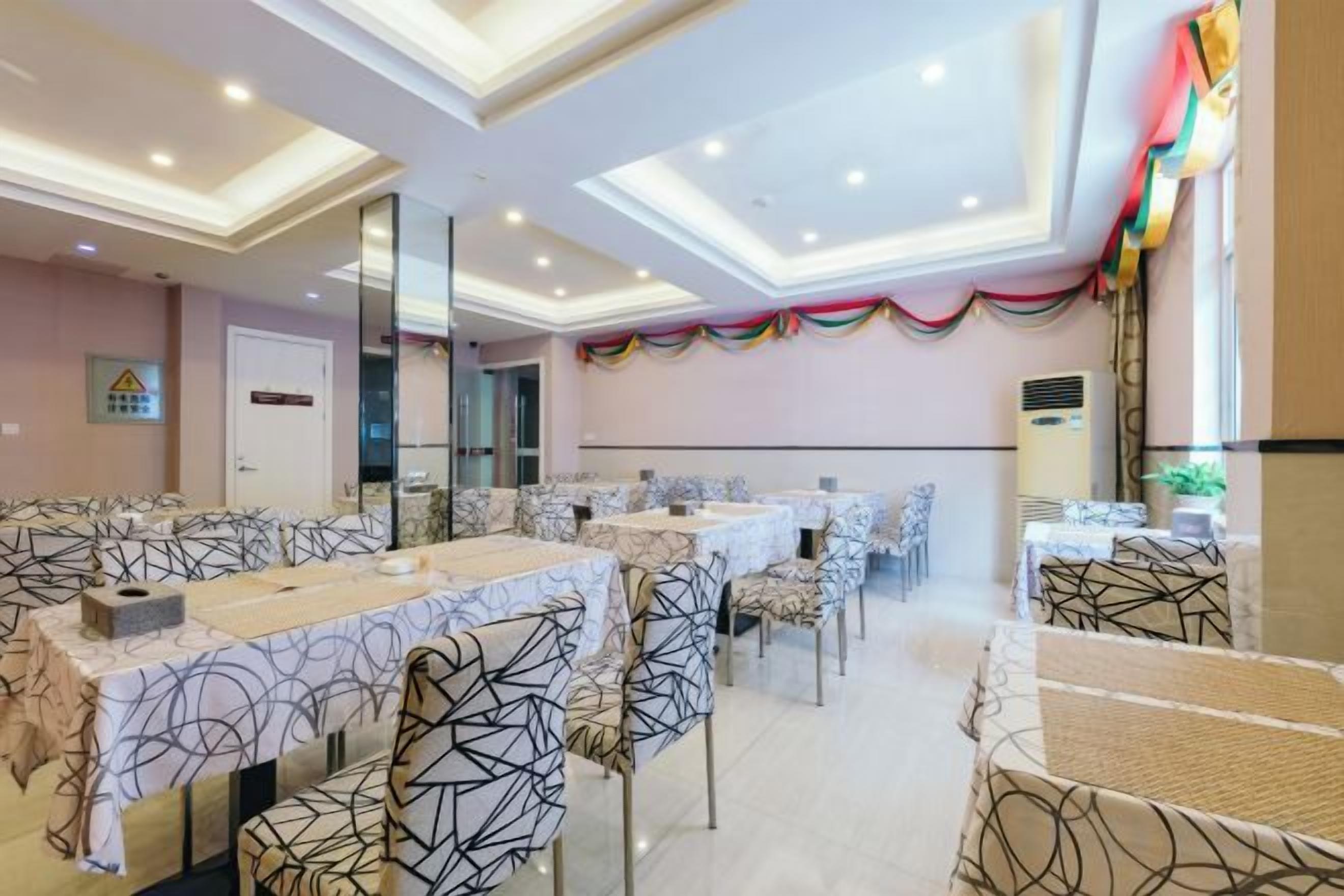 Um espaço de refeições de hotel com várias mesas e cadeiras, uma parede espelhada e um teto com iluminação embutida.