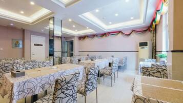 Um espaço de refeições de hotel com várias mesas e cadeiras, uma parede espelhada e um teto com iluminação embutida.