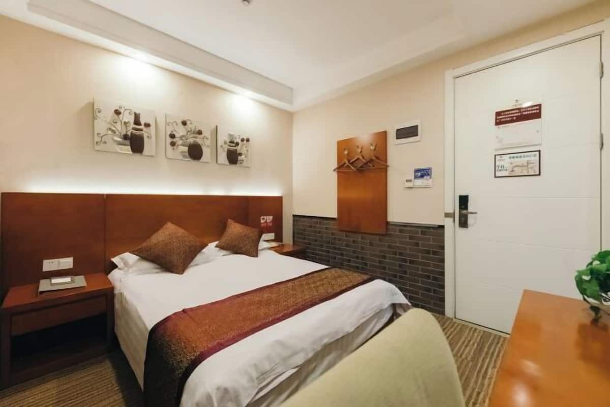 A hotel room with a bed, a nightstand, a desk, a chair, a door, and wall decorations.