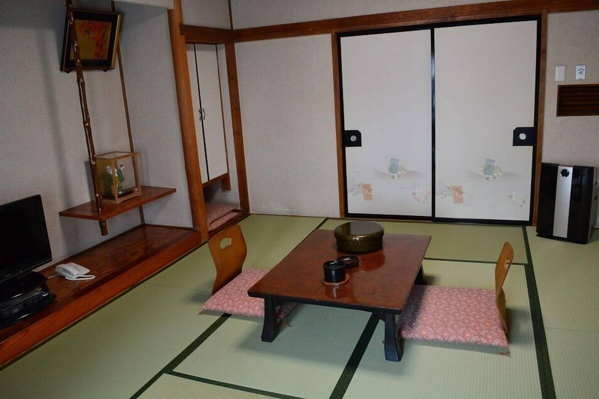A traditional Japanese room with tatami flooring, a low table with a bowl, a television, and a sliding door.