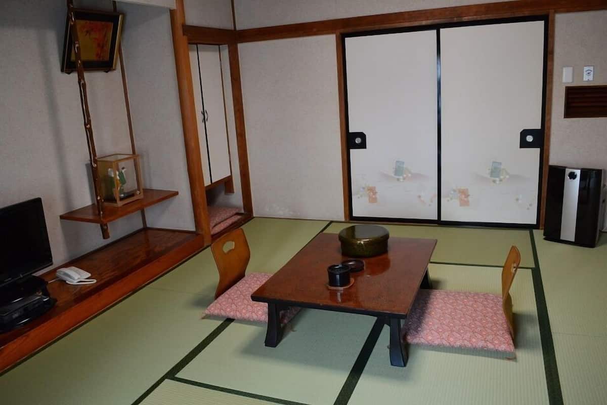 A traditional Japanese room with tatami flooring, a low table with a bowl, a television, and a sliding door.