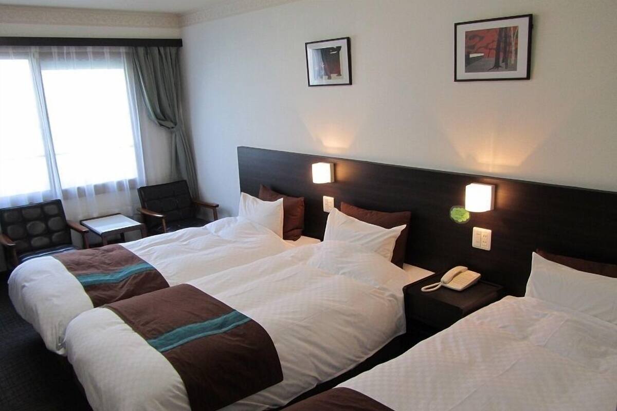 A hotel room with two beds, a desk, a chair, and two wall-mounted lamps.