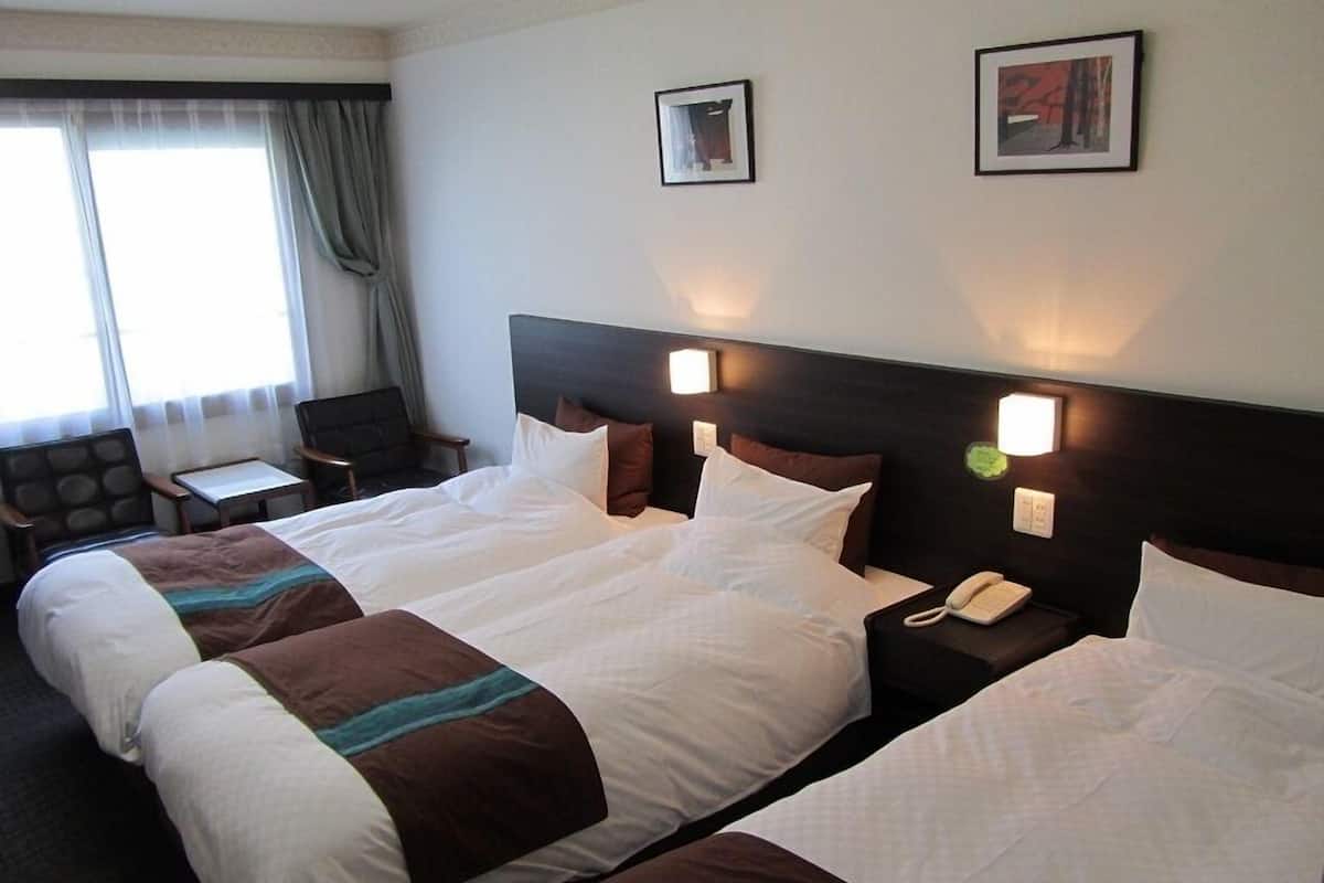 A hotel room with two beds, a desk, a chair, and two wall-mounted lamps.