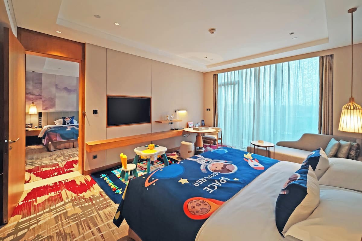 Ein Hotelzimmer mit Bett, Schreibtisch, Stuhl, Fernseher und einem großen Fenster.