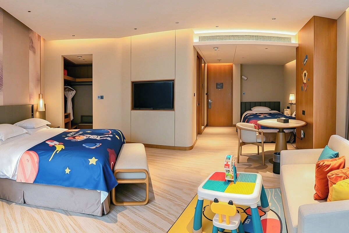 A hotel room with a bed, a desk, a chair, a small table, and a television.
