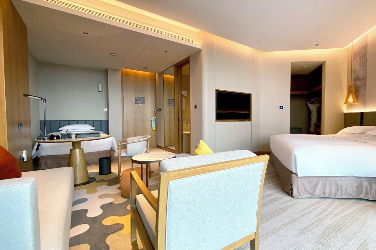 Habitación de hotel con cama, escritorio, silla, espejo y televisión.