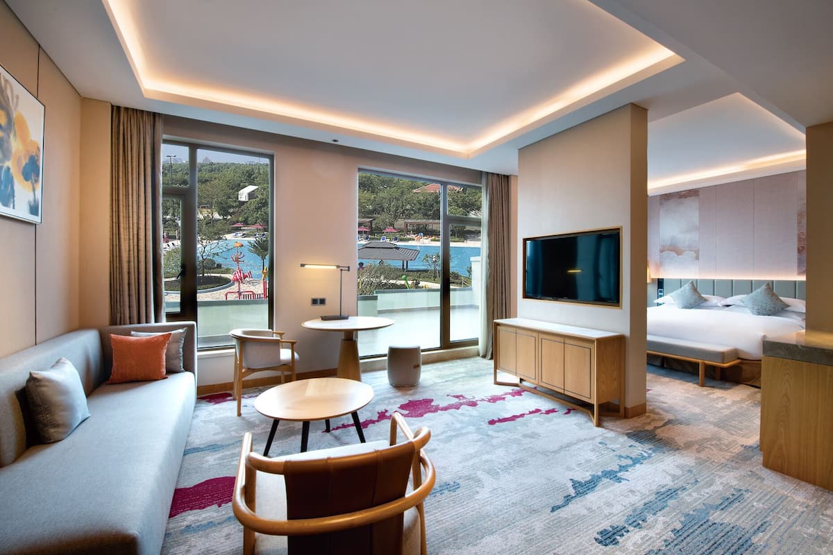 A modern hotel room with a sofa, a dining table, a TV, and a bed.