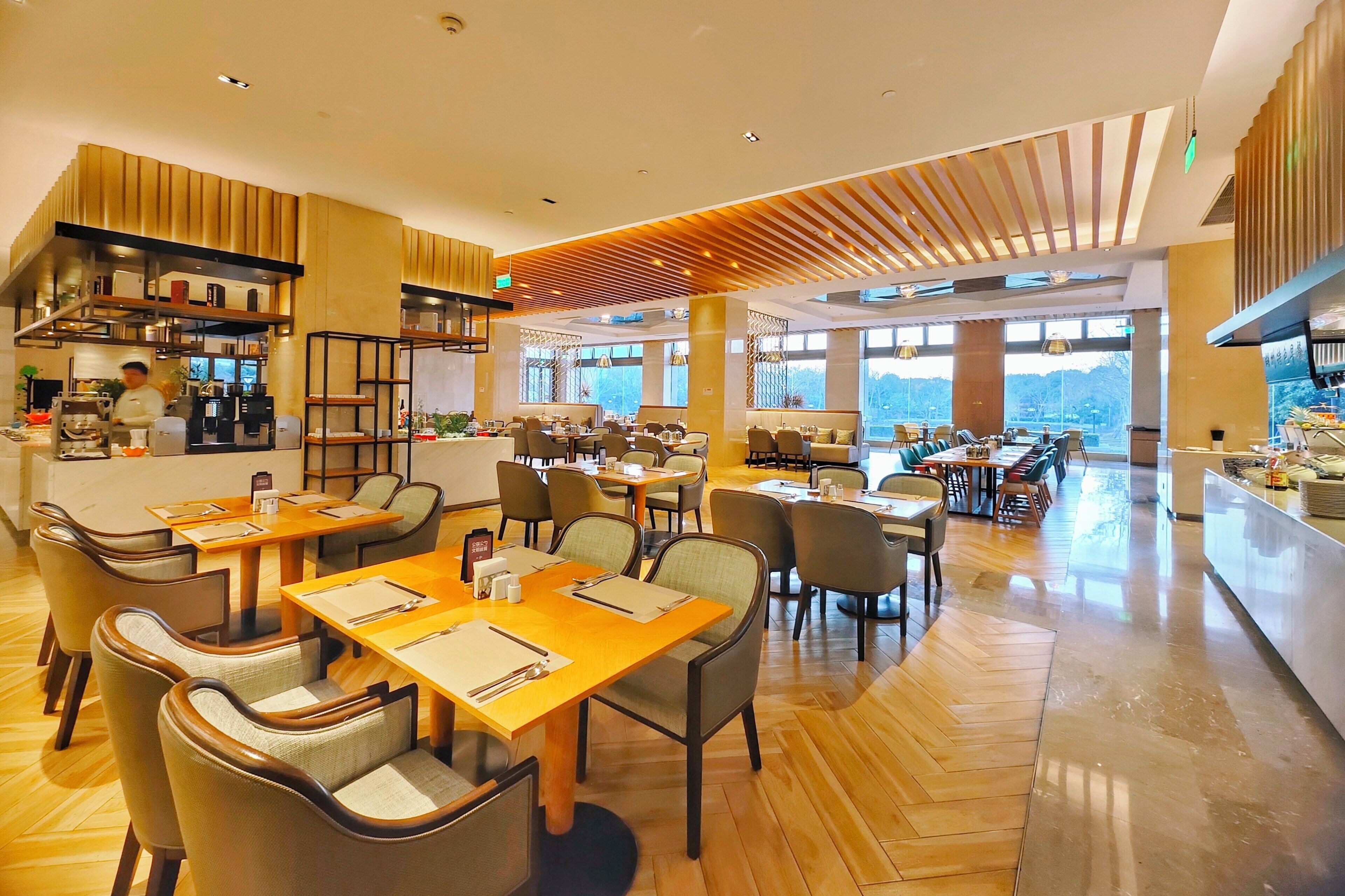 A modern restaurant with wooden flooring, multiple dining areas, and large windows offering a view of the outdoors.