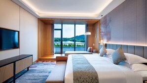 Une chambre d’hôtel moderne dotée d’un grand lit, d’une télévision à écran plat, d’un bureau et offrant une vue sur un lac et des montagnes.