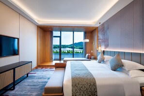 Een moderne hotelkamer met een groot bed, een flatscreen televisie, een bureau en uitzicht op een meer en bergen.