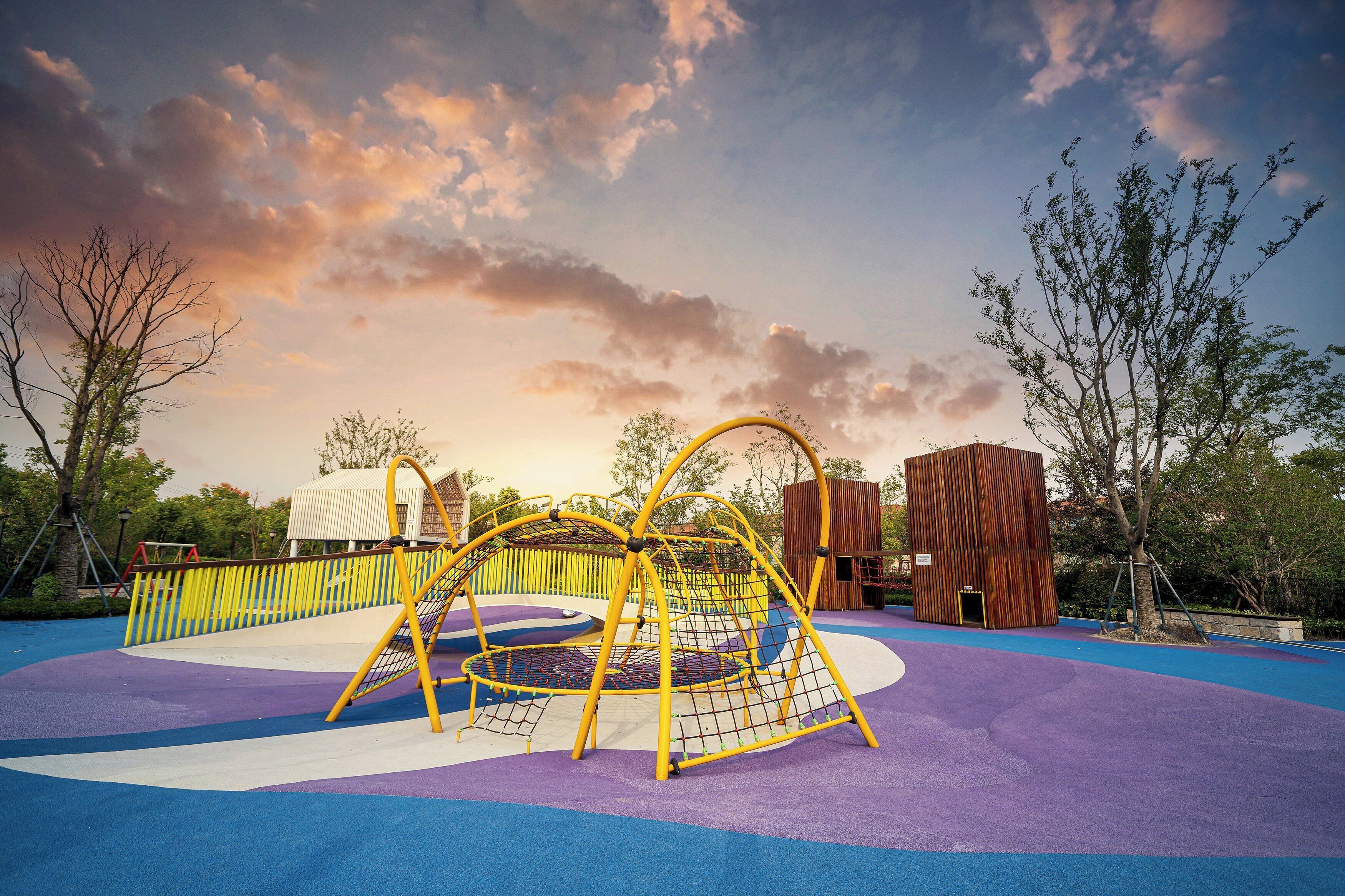 A playground with a climbing structure, a wooden playhouse, and a fenced area.
