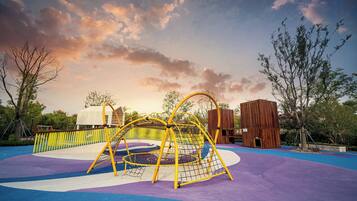A playground with a climbing structure, a wooden playhouse, and a fenced area.