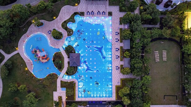 Vue aérienne d’un complexe de piscines comprenant plusieurs bassins, des espaces de détente et une végétation luxuriante.