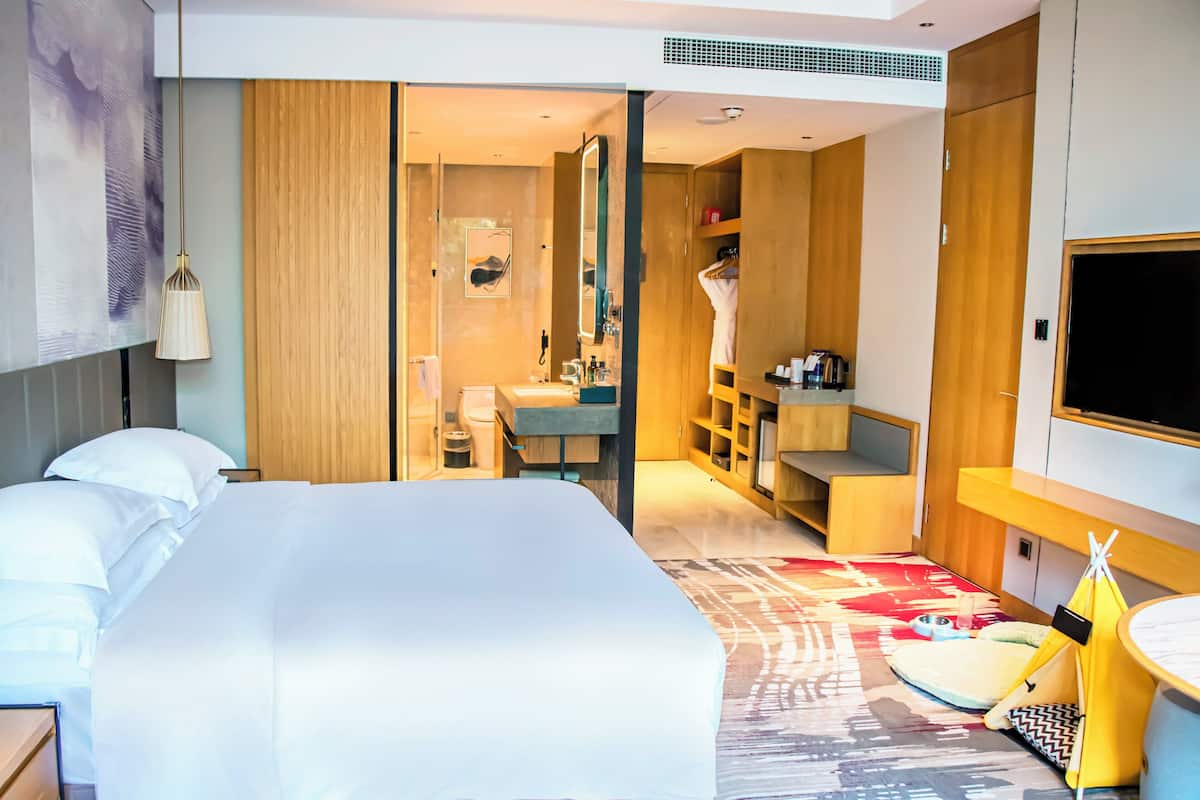 Ein modernes Hotelzimmer mit einem großen Bett, einem Badezimmer mit Spiegel und Waschbecken, einem Fernseher und einer gelben, tentartigen Struktur.