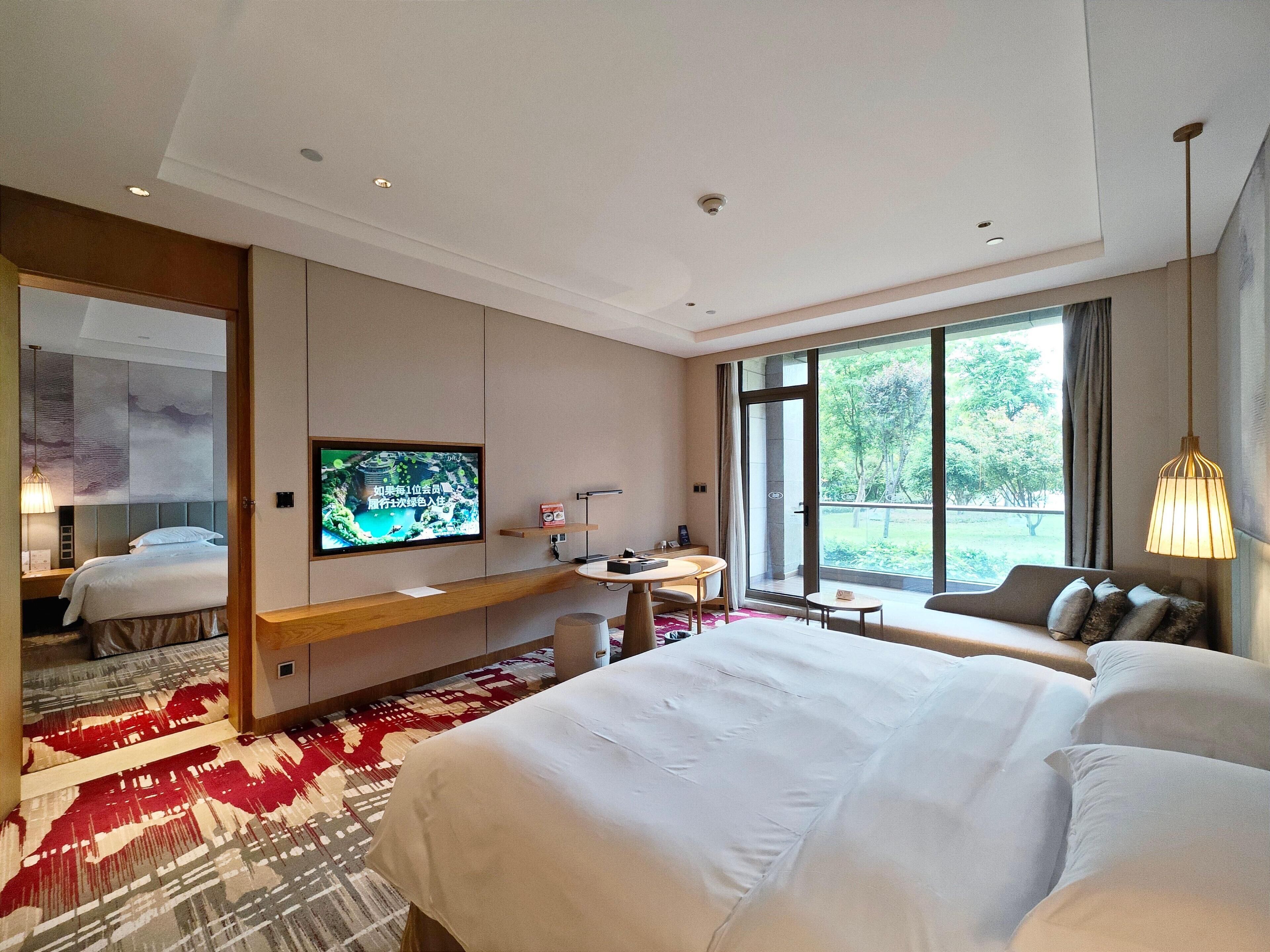 Une chambre d’hôtel avec un grand lit, une télévision, un bureau avec une chaise, une petite table et un canapé.