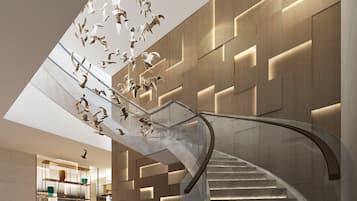 A modern interior with a curved staircase, a glass railing, and a wall with geometric patterns.