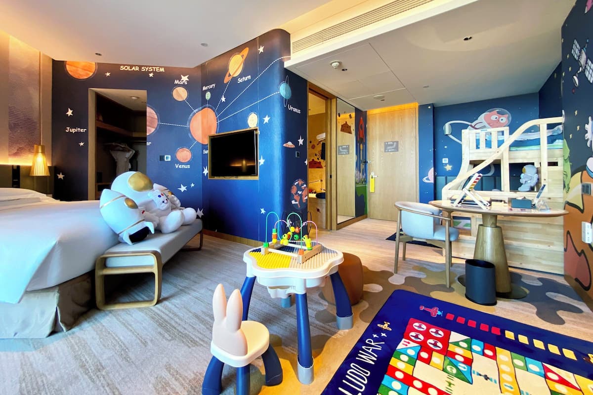 Ein Kinderzimmer mit Bett, Schreibtisch, Spielbereich und Wandmalerei mit dem Sonnensystem.