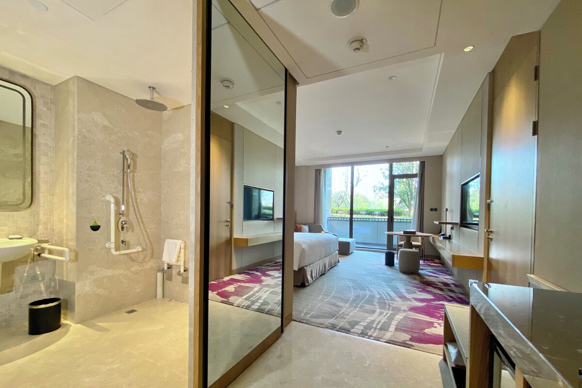 Ein modernes Hotelzimmer mit Dusche, einem Bett, einem Fernseher und einem Balkon mit Blick.